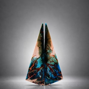 Puede incluir: Dos piezas de arte triangulares con un diseño veteado. Las piezas están una al lado de la otra, creando una forma simétrica. Los colores incluyen tonos de azul, turquesa, marrón y rosa, con patrones rojos en forma de vetas. Los bordes superiores son azul claro.