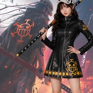Puede incluir: Chaqueta negra de cuero sintético con cremallera, mangas largas y falda acampanada. La chaqueta presenta detalles dorados y un diseño gráfico. Se sostiene un bastón negro y dorado. Una persona lleva un sombrero con un patrón en blanco y negro.