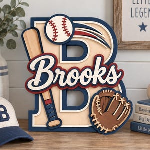 Op de afbeelding: Een gelaagd houten letter B-bord met de naam Brooks in cursief schrift, een honkbalknuppel, een honkbal en een bruine honkbalhandschoen. Het ontwerp gebruikt marineblauw, crème en rood, met de naam Brooks prominent in het midden weergegeven.