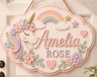 May include: A cloud-shaped wooden wall sign featuring a unicorn with a pastel mane, a rainbow, stars, and hearts. The name Amelia ROSE is written in raised lettering. The sign is decorated with floral accents and hangs from a jute rope.