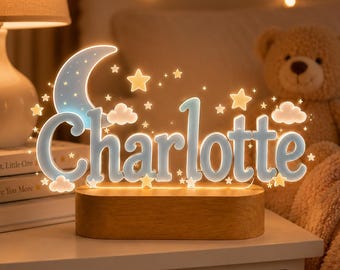 May include: A custom LED night light featuring the name Charlotte in light blue, illuminated letters. The design includes a crescent moon, small stars, and clouds, all mounted on a rectangular wooden base that glows with warm light.