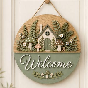 May include: A circular wooden wall sign featuring a layered design with a cottage, ferns, mushrooms, and daisies. The bottom half is painted sage green with the white script text Welcome, accented by small mushroom and leaf cutouts at the base.