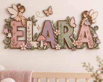 May include: A wall-mounted wooden name sign spelling ELARA in multi-colored block letters. The design features two illustrated fairies with wings, butterflies, small mushrooms, and various floral accents in soft pastel shades of pink, purple, and green.