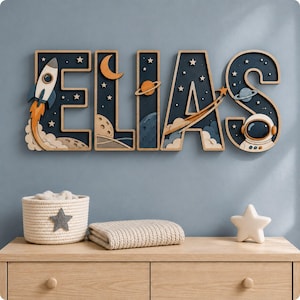 Puede incluir: Un letrero de madera para pared que deletrea el nombre ELIAS en letras grandes. Cada letra presenta un fondo azul oscuro con temática espacial y recortes en capas de un cohete, una luna creciente, planetas, estrellas y un casco de astronauta.
