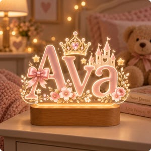 May include: A custom light-up sign featuring the name Ava in soft pink letters, accented with a gold crown, a castle, a pink bow, and floral details. The acrylic display is illuminated from within and mounted on a smooth, oval-shaped wooden base.