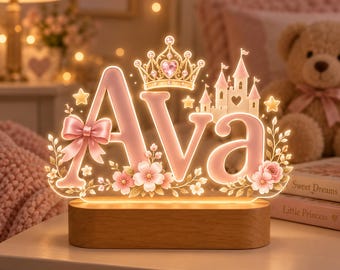 May include: A custom light-up sign featuring the name Ava in soft pink letters, accented with a gold crown, a castle, a pink bow, and floral details. The acrylic display is illuminated from within and mounted on a smooth, oval-shaped wooden base.
