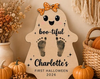 May include: A light-colored wooden ghost-shaped sign featuring an orange polka-dot bow, black eyes, a smiling mouth, and two black baby footprints. The text reads "boo-tiful", "Charlotte's", "FIRST HALLOWEEN", and "2026" with small star accents.