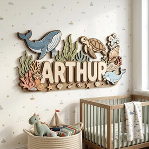 Puede incluir: Arte mural de madera con el nombre "ARTHUR" y criaturas marinas: ballena, tortuga y delfín. La obra incluye corales, algas y conchas, creando un tema náutico. Ideal para una habitación infantil.