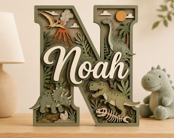 May include: A layered wooden letter N featuring a dinosaur theme with a volcano, a pterodactyl, a triceratops, a brachiosaurus, a T-Rex, and a fossil skeleton. The name Noah is written in white script across the center of the green letter.