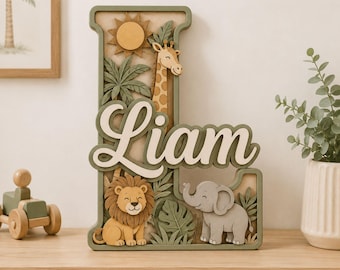 May include: A layered wooden letter L featuring the name Liam in white script. The design includes a yellow sun, a giraffe, a lion, and an elephant surrounded by green palm leaves. The color palette consists of muted greens, tans, and yellows.