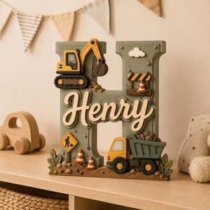 May include: A sage green decorative letter H featuring a construction theme with a yellow excavator, a dump truck, traffic cones, a road work sign, and a small white cloud. The name Henry is written in raised cream-colored script across the center.