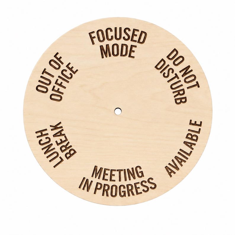 May include: A circular light-colored wooden status indicator sign featuring a central hole and laser-engraved text. The text options arranged around the center are FOCUSED MODE, DO NOT DISTURB, AVAILABLE, MEETING IN PROGRESS, LUNCH BREAK, and OUT OF OFFICE.