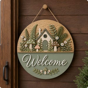 May include: A circular wooden wall sign featuring a layered design with a small house, mushrooms, ferns, and daisies. The bottom half is painted sage green with the white script text Welcome and small mushroom accents hanging from a jute twine loop.