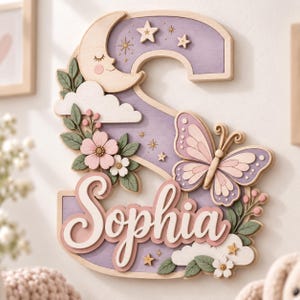 Könnte beinhalten: Ein dekoratives Wandschild aus Holz in Form des Buchstabens S, bemalt in Lavendel und Creme. Es zeigt eine Mondsichel, Sterne, einen Schmetterling, Wolken und florale Akzente. Der Name Sophia ist in weißer Schreibschrift mittig angebracht.