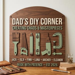May include: Wooden sign with the text "DAD'S DIY CORNER" and "CREATING CHAOS & MASTERPIECES". The sign features tool illustrations in green and brown. Below are names and the text "MADE WITH PATIENCE - EST 2026".
