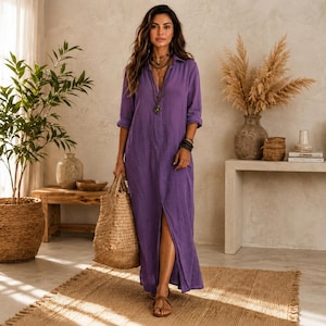 May include: A long-sleeved, floor-length purple button-down shirt dress with a collar and a front slit. The dress features a relaxed fit, long sleeves with cuffs, and a button placket extending down the front. It is paired with a large woven straw tote bag.