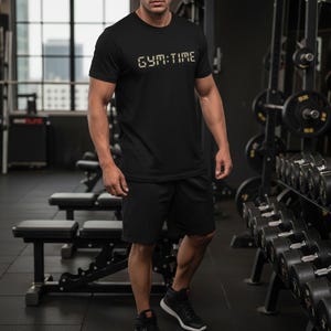 以下が含まれることがあります： 胸元にデジタル時計風のフォントで「GYM:TIME」という文字がプリントされた黒の半袖Tシャツと、黒のスポーツショーツ。Tシャツはクルーネックで、無地の黒い生地を使用したスタンダードなフィット感のデザインです。