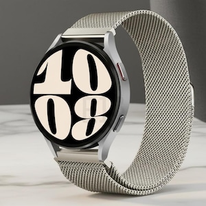 May include: Silver smartwatch with a mesh strap showing the time 10:08 on a black screen. The watch has a round face with a silver bezel and two buttons. The strap is a light silver colour.