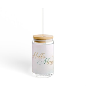 Könnte beinhalten: Ein durchsichtiger Glasbecher mit Bambusdeckel und einem durchsichtigen Strohhalm. Auf dem Becher steht in goldener und teal-farbener Schrift "Hello May". Der Becher ist für kalte Getränke konzipiert.