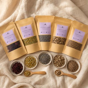 Könnte beinhalten: Fünf Kraftpapierbeutel mit getrockneten Kräutern, beschriftet als Hibiscus Flowers, Chamomile Flowers, Lavender Flowers, Dandelion Roots und Valerian Root, dazu passende kleine Schalen mit den Kräutern und zwei Holzlöffel.