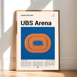 May include: A framed poster featuring the text "UBS Arena" above a blue and orange stadium illustration. The poster includes the text "Elmont, New York" and a hockey stick graphic. The poster is leaning against a white wall and wooden floor.