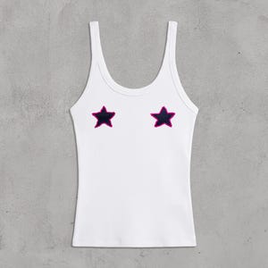 Può includere: Canotta bianca a coste con due applicazioni a forma di stella blu scuro bordate di rosa. La canotta ha uno scollo tondo e spalline sottili. Il testo "bb.projectlab" è stampato in basso a sinistra.