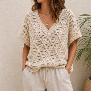 May include: Cream-colored, short-sleeved crochet top with a V-neck and diamond pattern. The top is paired with light-colored linen pants. The overall aesthetic is casual and relaxed, suitable for warm weather.