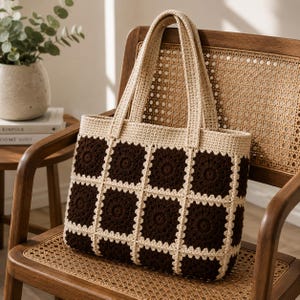 May include: A rectangular crochet tote bag featuring a checkerboard pattern of dark brown and cream-colored squares. The bag is constructed from joined granny squares with a cream-colored border and two matching cream-colored crochet handles.