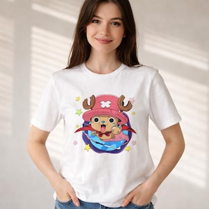 May include: White t-shirt featuring a cartoon character with a pink hat, brown antlers, and a red cape. The character is surrounded by colorful stars and a blue and purple background.