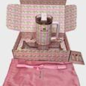 Puede incluir: Un termo de viaje de acero inoxidable con asa y tapa transparente, presentado en una caja decorativa con un estampado floral rosa y blanco. La caja tambi&eacute;n contiene una bolsa de sat&eacute;n rosa y una tarjeta peque&ntilde;a. El termo tiene una etiqueta verde y blanca.