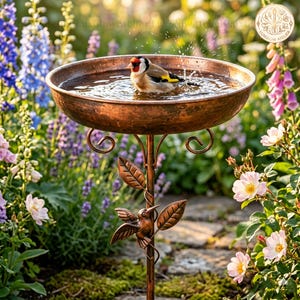 May include: A copper-colored metal birdbath featuring a wide, shallow basin supported by a slender stand. The stand is decorated with a sculpted metal hummingbird and several leaf accents. A small goldfinch is splashing in the water.