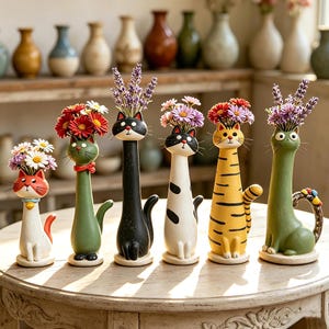 May include: A selection of decorative cat-shaped vases, each with a distinct design and colour palette. The vases are filled with vibrant flowers, creating a delightful arrangement. The cats are white, orange, green, black, and yellow, with various patterns.