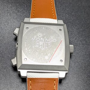 May include: A square silver-tone watch case with a tan leather strap. The case back features the text 1969-1979 SPECIAL EDITION, MONACO, HEUER, and ONE OF 169. Two pushers are on the left side, and a crown is on the right side of the watch case.