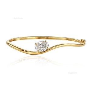 Puede incluir: Una pulsera dorada con un brillante diamante de talla ovalada. La pulsera tiene un diseño único y fluido, con el diamante engastado en el centro. El cierre es visible en el lado derecho. La joya se muestra sobre un fondo blanco.