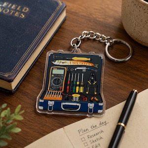 May include: A clear acrylic keychain featuring a graphic of an open blue tool case. Inside the case are a yellow digital multimeter, a silver fish lure, various screwdrivers with colored handles, pliers, a spool of wire, and a set of metal bits.