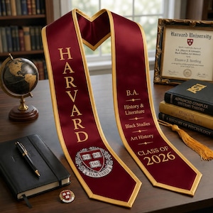Könnte beinhalten: Eine bordeauxrote Abschlussstola mit goldener Umrandung, die das Wort HARVARD in goldener Schrift, das Wappen der Harvard University und Text zu einem B.A. in Geschichte & Literatur, Black Studies und Kunstgeschichte für den Jahrgang 2026 zeigt.