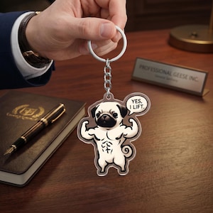 Può includere: Un portachiavi in acrilico trasparente con un carlino dei cartoni animati che mostra i suoi muscoli. Il carlino ha la faccia nera ed è bianco con un fisico muscoloso. Una nuvoletta dice "YES, I LIFT". Il portachiavi ha una catena e un anello argentati.