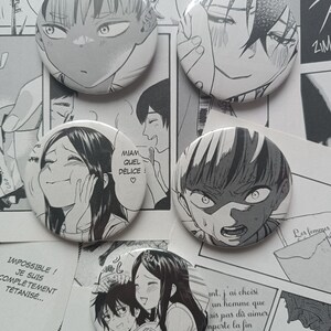 Puede incluir: Cinco chapas redondas con ilustraciones en blanco y negro estilo manga de personajes con diversas expresiones faciales. Las chapas están dispuestas sobre un fondo de páginas de cómic impresas con texto en francés visible por todas partes.