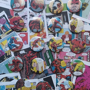 Könnte beinhalten: Eine Sammlung von siebzehn runden Ansteckbuttons mit verschiedenen farbenfrohen Comic-Illustrationen der Figur Daredevil in Action-Posen, platziert vor einem Hintergrund aus überlappenden Vintage-Comicseiten mit französischem Text.