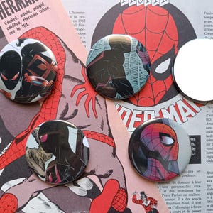 Könnte beinhalten: Vier runde Ansteckbuttons mit Illustrationen der Comicfigur Spider-Man. Drei Buttons zeigen verschiedene Spider-Man-Figuren in schwarzen, roten und blauen Anzügen, während ein Button ein schlichter, reflektierender silberfarbener Spiegel ist.