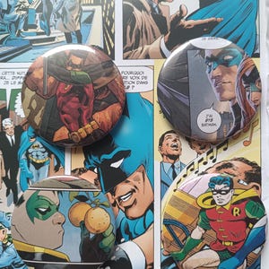 Könnte beinhalten: Vier runde Ansteckbuttons mit Comic-Illustrationen von Robin. Zwei Buttons zeigen Robin im rot-grünen Kostüm, einer zeigt eine Nahaufnahme von Robin mit Maske und einer zeigt Robin, wie er zwei Orangen hält. Die Buttons haben eine glänzende Oberfläche.