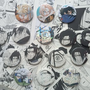 Könnte beinhalten: Eine Sammlung von vierzehn runden Ansteckbuttons mit verschiedenen Anime-Charakter-Illustrationen. Die Buttons zeigen unterschiedliche Ausdrücke und Szenen, darunter schwarz-weiße Manga-Kunst und farbenfrohe Porträts der Charaktere.