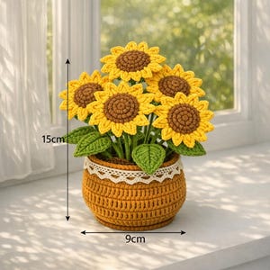 May include: A crocheted sunflower arrangement in a woven pot. The sunflowers have yellow petals and brown centres. The pot is 9cm wide and 15cm tall, with a white lace trim. Green leaves are visible.