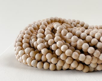 Puede incluir: Un montón de cuentas de madera natural de color beige claro. Las cuentas son redondas y lisas, y están dispuestas en un montón suelto.