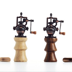 May include: Two antique-style wooden salt and pepper grinders with metal mechanisms. The grinders are made of light and dark wood and have a vintage look.