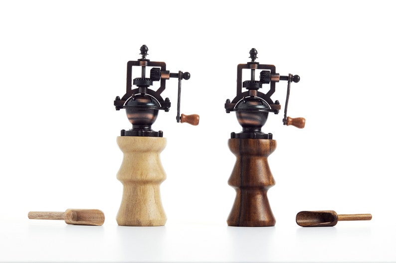 May include: Two antique-style wooden salt and pepper grinders with metal mechanisms. The grinders are made of light and dark wood and have a vintage look.