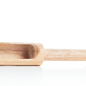 May include: A wooden scoop with a rounded handle. The scoop is made of light brown wood and has a smooth finish.