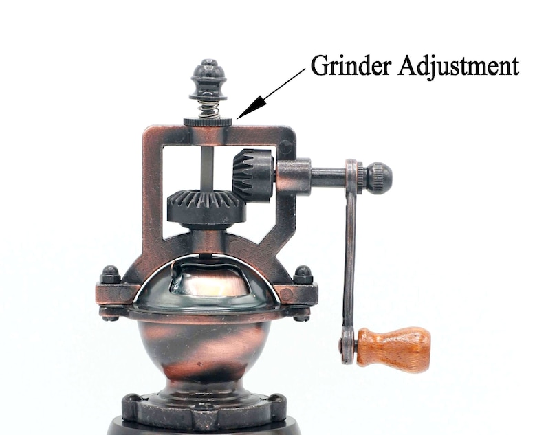 May include: A vintage-style manual coffee grinder with a copper finish. The grinder has a crank handle and a gear system for grinding coffee beans. The grinder has a knob on top for adjusting the grind size. The text "Grinder Adjustment" is visible in the image.