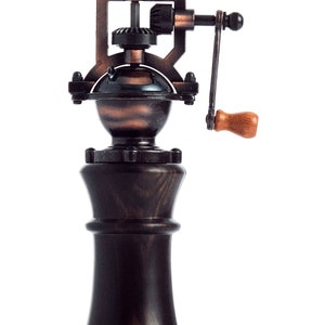 May include: A vintage-style manual coffee grinder with a wooden base and a copper-toned metal top. The grinder has a crank handle and a gear system visible on the top.