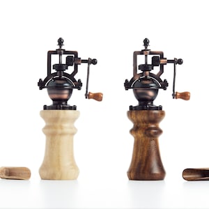 May include: Two antique-style wooden salt and pepper grinders with copper accents and wooden crank handles. The grinders are on a white surface.